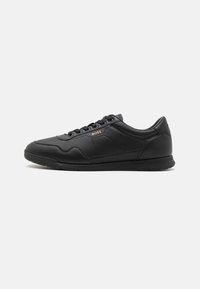 Black leather sneaker with a smooth texture, featuring a lace-up design, subtle branding, and a rubber sole with a patterned tread.