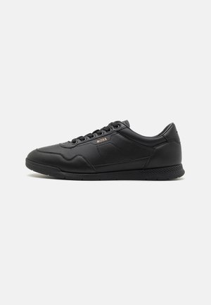 Black leather sneaker with a smooth texture, featuring a lace-up design, subtle branding, and a rubber sole with a patterned tread.