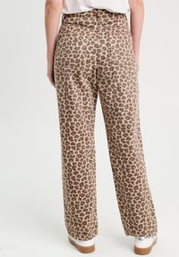 Beige weiter Hosen mit einem braunen Leopardenmuster, hoch geschnitten, mit zwei Gesäßtaschen und einer glatten Textur. Die Schuhe sind weiß mit einer braunen Sohle.