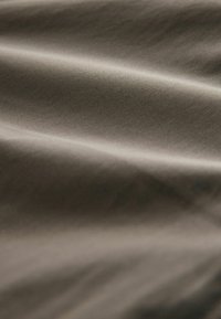 Gros plan d’un tissu lisse et doux avec de petits plis dans une couleur taupe neutre montrant la texture et une légère ombre.