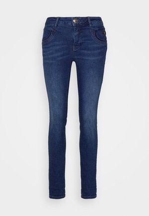 Jean skinny bleu foncé avec poches avant, passants de ceinture et fermeture par bouton en métal.