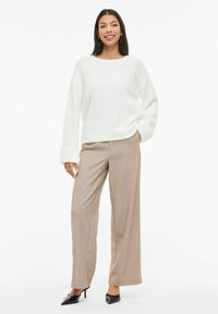 Biały, oversize'owy sweter z prążkowanymi mankietami, zestawiony z beżowymi spodniami o szerokich nogawkach i czarnymi szpilkami. Gładkie tekstury i luźny krój.