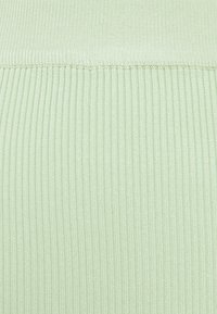 Ljusgrön ribbad tyg med en texturerad yta, med vertikala linjer och något varierande nyanser. Sömmar vid övre kanten är synliga.