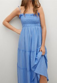 Robe maxi bleu à étages avec corsage smocké et bretelles ajustables. Fabriquée en tissu léger, elle présente un design fluide et une texture douce.