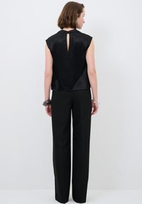 Top senza maniche in satin nero con dettaglio a chiave sul retro, abbinato a pantaloni neri a vita alta. Texture liscia, vestibilità rilassata e design minimal.