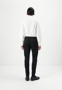 White long-sleeve shirt paired with black trousers, featuring a fitted design and back pockets, complemented by black shoes.
