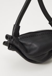 Black leather handbag featuring soft, textured leather, a gathered design, short handles, and visible stitching details.