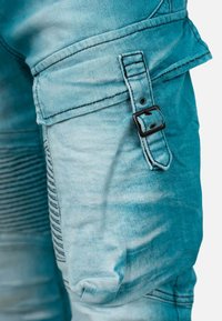 Pantalons cargo en denim bleu clair avec une poche latérale dotée d'une boucle noire et de détails de couture. Texture lisse avec une finition délavée.