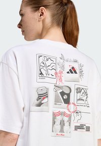 Bijela pamučna majica s raznim crnim i crvenim grafičkim otiscima, uključujući ilustracije sporta i prirode na leđima.