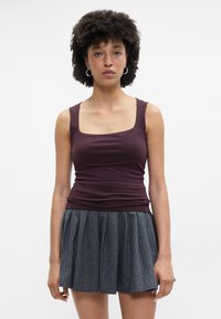 Μπορντώ τοπ με τετράγωνη λαιμόκοψη και εφαρμοστό σχέδιο, συνδυασμένο με πλισέ γκρι μίνι φούστα με κάθετες ρίγες.