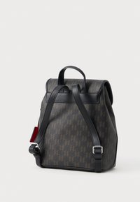 Petit sac à dos marron avec des bretelles noires réglables et un motif géométrique sombre, posé debout sur un fond blanc.