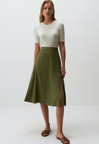 Zielona spódnica midi z bocznym rozcięciem, wykonana z lekkiego materiału. W zestawie z białym, prążkowanym topem i brązowymi klapkami. Gładka tekstura.