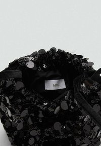 Černá taška zdobená lesklými černými flitry, s měkkou látkovou podšívkou a stahovací šňůrkou. Vnitřní štítek uvádí "MNG."