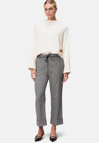 Cremefarvet ribstrikket sweater med brede ærmer, parret med grå ternede bukser med snøre i taljen og opkrøllede manchetter. Sorte spidse flade sko.
