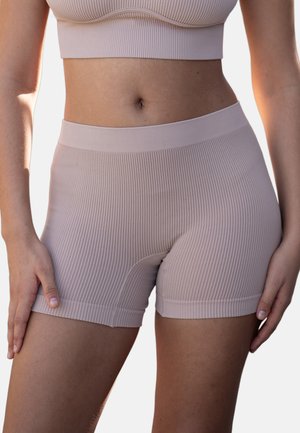 Woman wearing beige ribbed high-waist biker shorts and matching sports bra, hands resting on thighs, standing against a plain background.