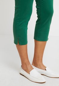 Pantalons courts verts à coupe ajustée, texture lisse, avec de petites fentes latérales et des boutons décoratifs à l'ourlet.