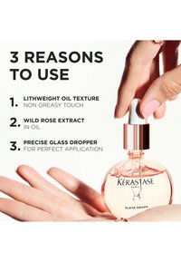 Kérastase Glaze Drops en una botella redonda de vidrio con aceite de color rosa claro, tapa gotero blanca, sostenida en una mano con uñas manicuras.