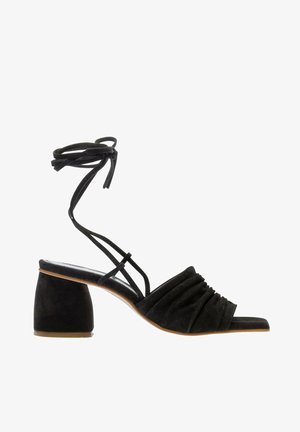 Czarne zamszowe sandały na obcasie z marszczonym designem, otwartym noskiem i paskiem wokół kostki. Blokowy obcas i gładka tekstura podkreślają ogólny wygląd.