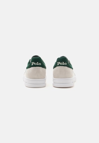 Paire de baskets blanches avec languettes de talon vertes, panneaux arrière en daim beige et logo "Polo" en lettres blanches sur chaque talon.