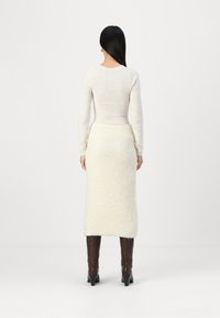 Un pull blanc et une jupe fourreau beige en peluche arrivant au genou, portés avec des bottes marron montantes. La tenue présente des manches longues et une silhouette ajustée.