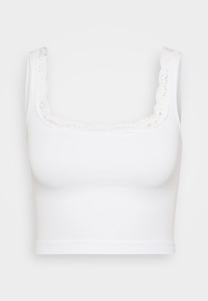 Vit kort topp i mjukt material med en scalloped spetskant längs halsringningen och tjocka axelremmar.