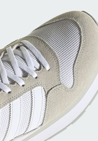 Baskets en daim beige et mesh blanc avec lacets blancs et trois bandes en cuir blanc sur le côté.