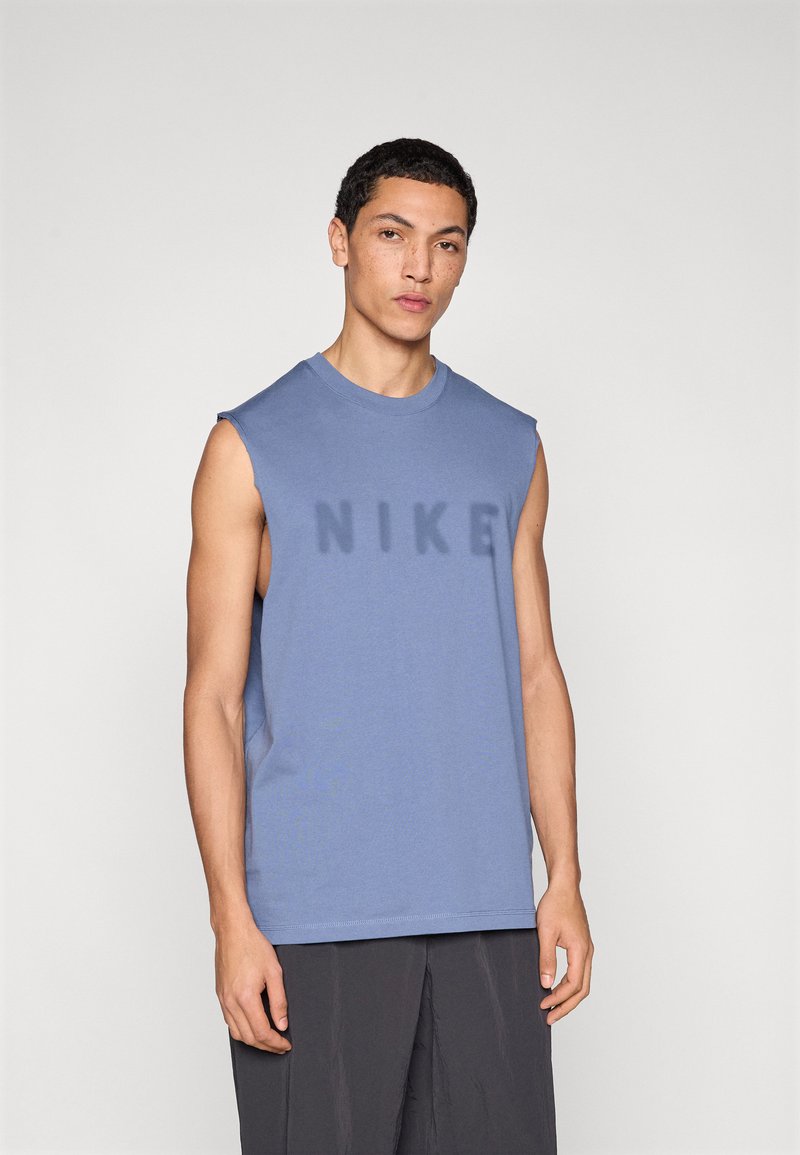 Ανοιχτό μπλε αμάνικο μπλουζάκι Nike με στρογγυλή λαιμόκοψη, που διαθέτει ένα ελαφρώς μεγαλύτερο, σκούρο μπλε λογότυπο "NIKE" στο μπροστινό μέρος. Απαλή υφή υφάσματος.