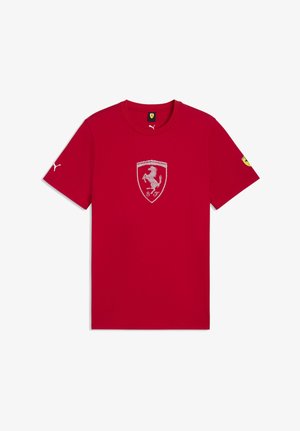 Camiseta roja de manga corta con cuello redondo, con un logo blanco de Puma en la manga derecha, un escudo de Ferrari en el centro y un parche amarillo de Ferrari en la manga izquierda.