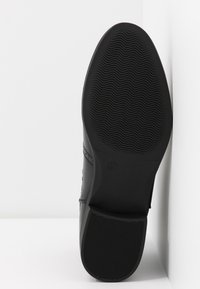 Suola di scarpa nera con una texture ondulata e una presa decorata. Presenta un bordo liscio e leggermente rialzato e un'impronta del logo.