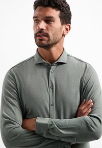 Langarm gestreept overhemd in een gedempte groene stof, met een gestructureerd patroon, knoopsluiting aan de voorkant met bijpassende knopen en aansluitende manchetten.