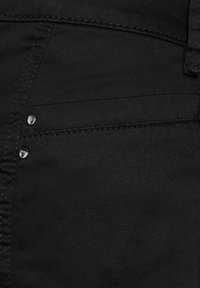 Jeans de mezclilla negros con una textura suave, diseño clásico de cinco bolsillos y remaches plateados decorativos cerca del bolsillo delantero.