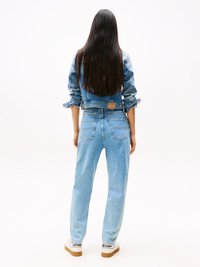 Salopetă din denim bleu deschis, cu mâneci lungi, talie strânsă și picioare ampla. Conține buzunare și o etichetă pe spate. Poartă cu teniși albi.