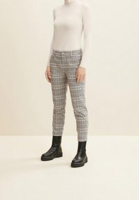 Halsen är hög på en beige topp som bärs med rutiga grå byxor, som har en smal passform, och svarta ankelboots med tjocka sulor.