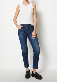 Vit ärmlös topp i kombination med mörkblå denimjeans med fem fickor och en smal rak passform. Svarta klackloafers.