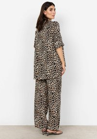 Bež i crni leopard uzorak dvodijelni outfit, koji se sastoji od slobodnog košulje s uvrnutim rukavima i širokih hlača.