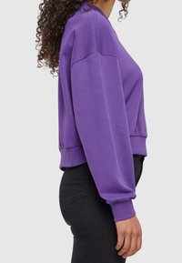 Felpa viola con scollo rotondo, spalle scese e polsini a costine. Il materiale sembra morbido; design cropped con una vestibilità rilassata.