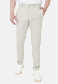 Pantaloni beige su misura con una texture liscia, tasche davanti e chiusura a un bottone. Abbinati a scarpe da ginnastica bianche con suole in gomma.