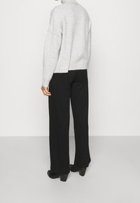 Maglione grigio chiaro a maglia con collo alto e spalle cadenti, abbinato a pantaloni neri a gamba larga e stivali neri con tacco.