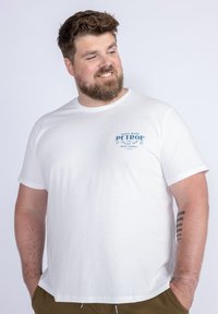 Bílý bavlněný tričko s modrou grafickou potiskem na levém prsu. Krátké rukávy s kulatým výstřihem, volný střih a měkký materiál.