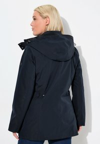 Marinblå vattentät jacka med huva, justerbara dragsko, sidofickor och en smidig, slät yta med minimal detaljer.