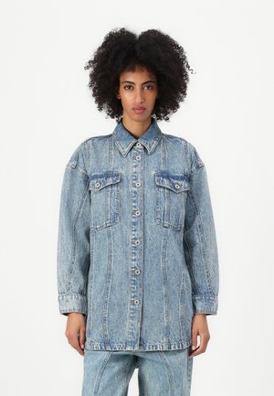 Light blue denim jacket with a pointed collar, two chest pockets, and a button-down front. Features a loose fit and visible stitching details.
