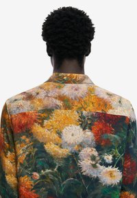 Camicia con stampa floreale dal design colorato che presenta fiori gialli, bianchi e rossi. Realizzata in tessuto testurizzato, è dotata di colletto e chiusura con bottoni.