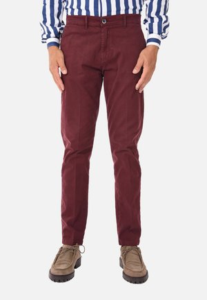 Chino in cotone color bordeaux con design slim fit, dotati di chiusura con bottone frontale e tasche laterali, abbinati a scarpe color marrone chiaro.