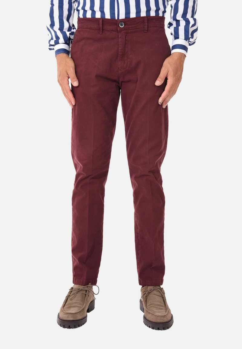 Chino in cotone color bordeaux con design slim fit, dotati di chiusura con bottone frontale e tasche laterali, abbinati a scarpe color marrone chiaro.