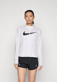 White Nike zip-up jacket with a black swoosh logo and long sleeves, paired with black basketball-style shorts featuring a small white logo.