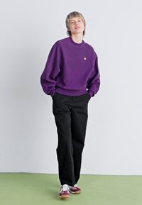 Lilla sweatshirt med en afslappet pasform, sorte bukser og multicolor sneakers. Glat tekstur, enkelt design og minimal brandingdetalje.