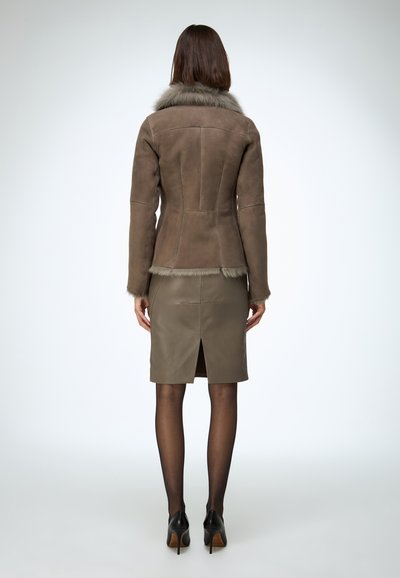 Veste en daim marron avec un col en fourrure grise, coupe ajustée, et une jupe en cuir assortie avec une fente au dos. Chaussures noires à talons hauts.