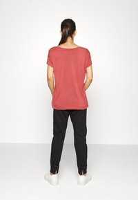 Camisa vermelha de manga curta com um corte solto, combinada com calças pretas ajustadas que têm detalhes em laço nos tornozelos e ténis brancos.