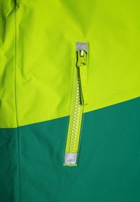 Tessuto colorato verde e lime a blocchi con tasca verticale con zip e nastro riflettente in cima e in fondo.