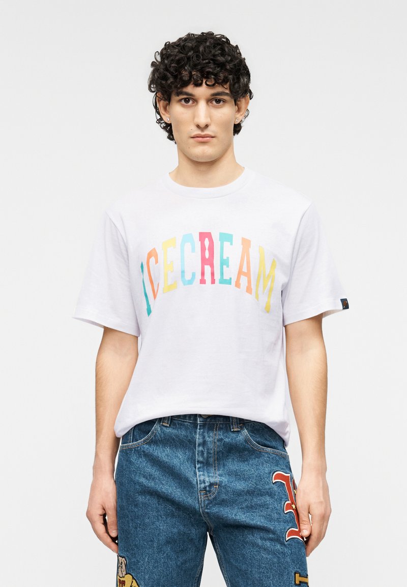 Άσπρο κοντομάνικο μπλουζάκι με πολύχρωμα γράμματα που σχηματίζουν τη λέξη "ICECREAM." Συνδυάζεται με μπλε τζιν τζινάκια με μπαλώματα.